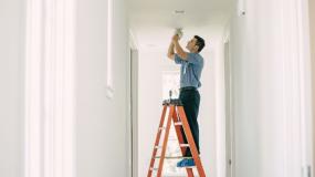 Mr. Electric electrician fixing a ceiling light while standing on a ladder.