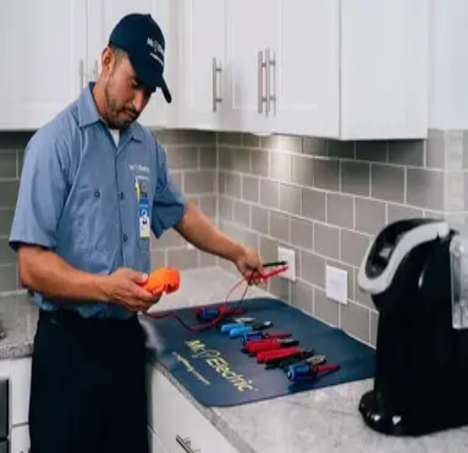 A Mr. Electric Electrician Stands at a Counter with Tools Spread Out on it and Uses a Device to Test an Electrical Outlet.