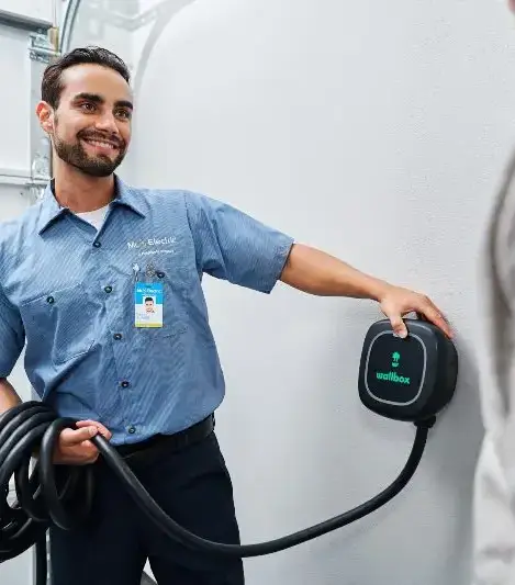 A Mr. Electric Electrician Holds a Coiled Cord Attached to an EV Charger on the Wall and Touches it to Show How to Use It