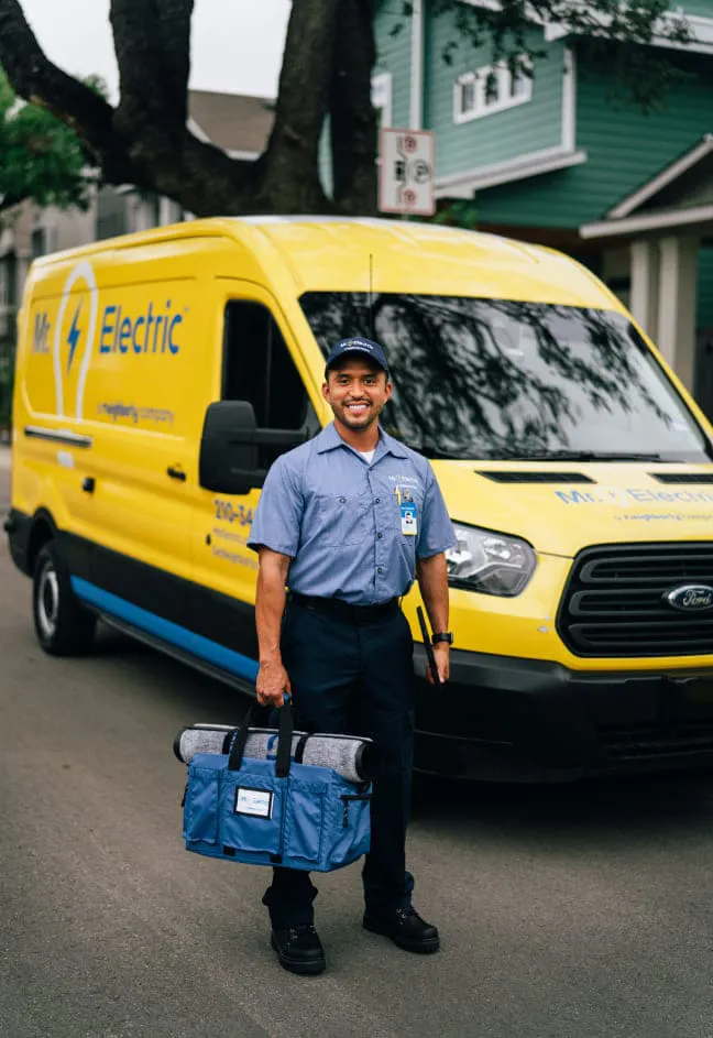 Smiling male Mr. Electric employee standing beside yellow branded van.