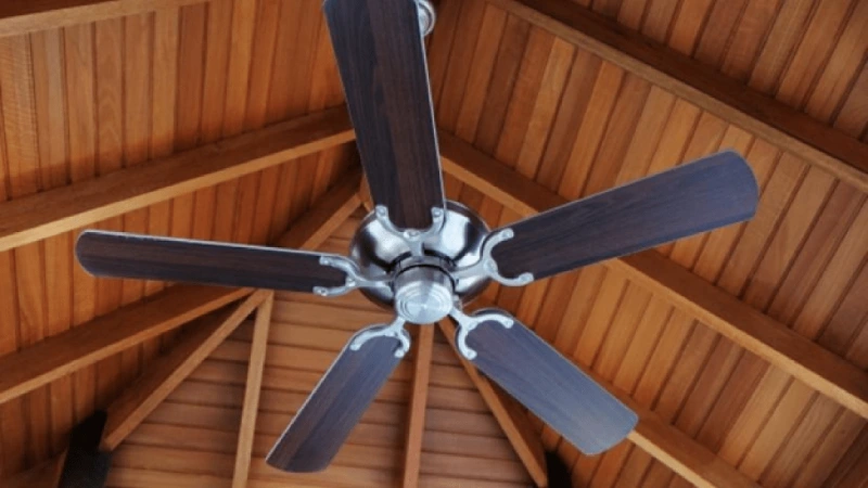 Ceiling fan with brown blades mounted on a high ceiling made of wood.