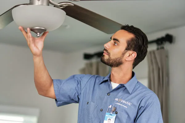 A Mr. Electric Service Professional Reaches Up to a Light Fixture Attached to a Ceiling Fan