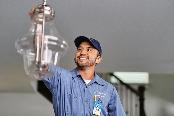A Smiling Mr. Electric Service Professional Reaches for a Pendant Light Fixture Suspended from a Ceiling