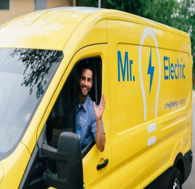 Mr. Electric electrician in a yellow van waves his arm out of the open driver-side window.