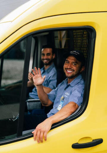 Two Mr. Electric technicians sitting in the yellow Mr. Electric van while waving and smiling. 