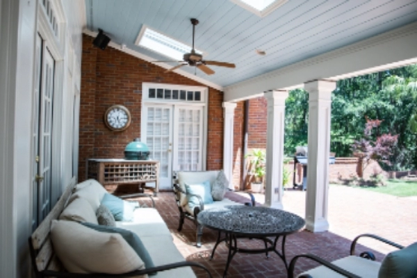 Outdoor patio area of a residential home with furniture, ceiling fan, and white French doors. 