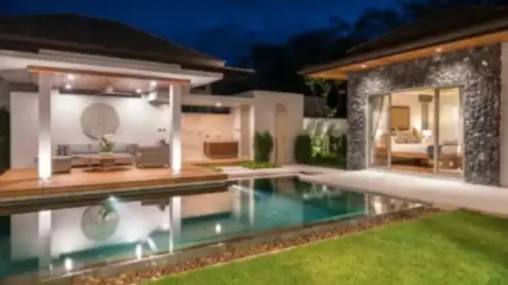 Backyard view of a residential home with beautiful outdoor lighting and pool.