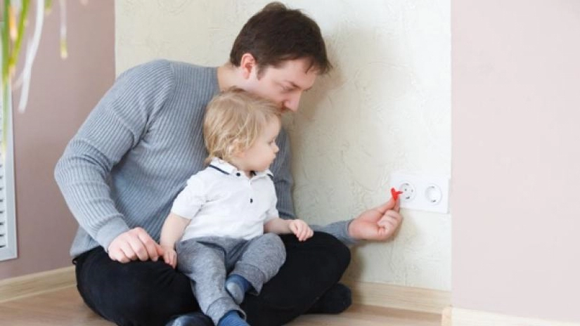 Dad putting child protector on outlet with baby watching.