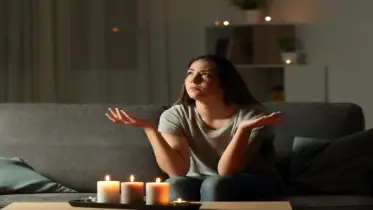 Woman with hands held out sitting on a couch in the living room at home with candles burning during a blackout.