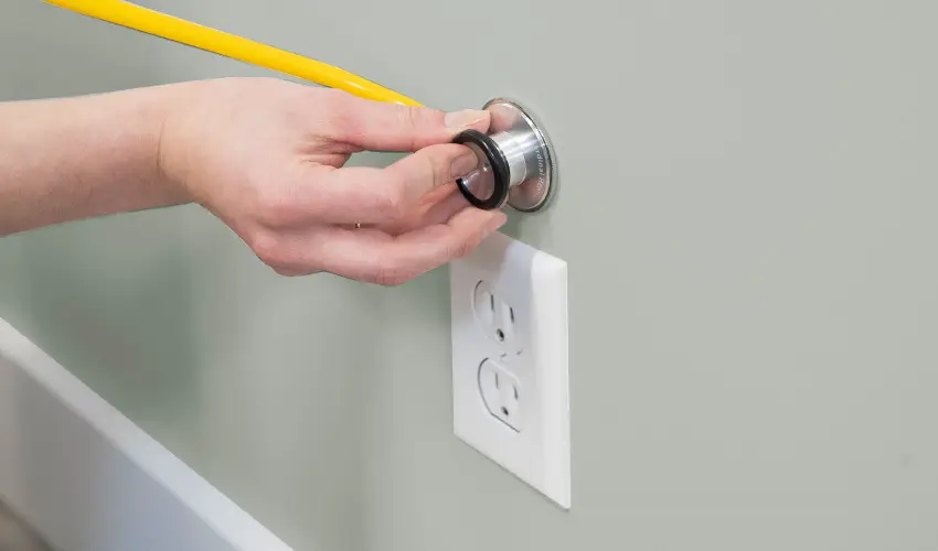 Hand holding stethoscope to wall.