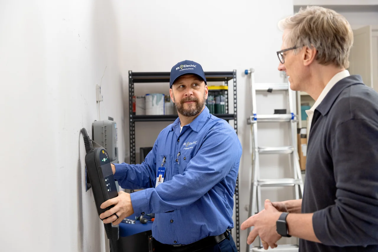 Professional electrician explaining an EV charger installation to a homeowner in a garage