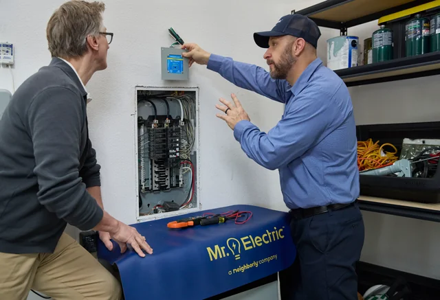 Professional electrician explaining an electrical panel and surge protector to a homeowner