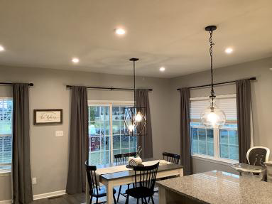 Several different hanging and recessed lights in a dining room and kitchen where new light installation has recently been completed.