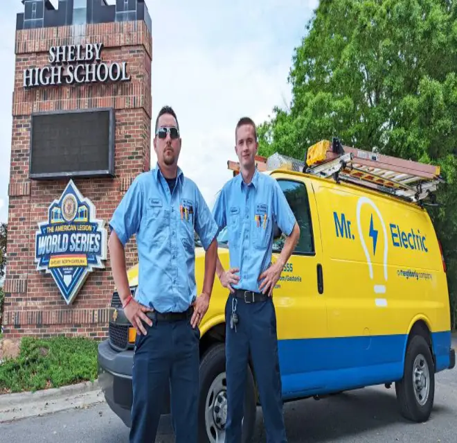 Two Mr. Electric of Gastonia specialists standing in front of the Shelby High School sign and their service truck.