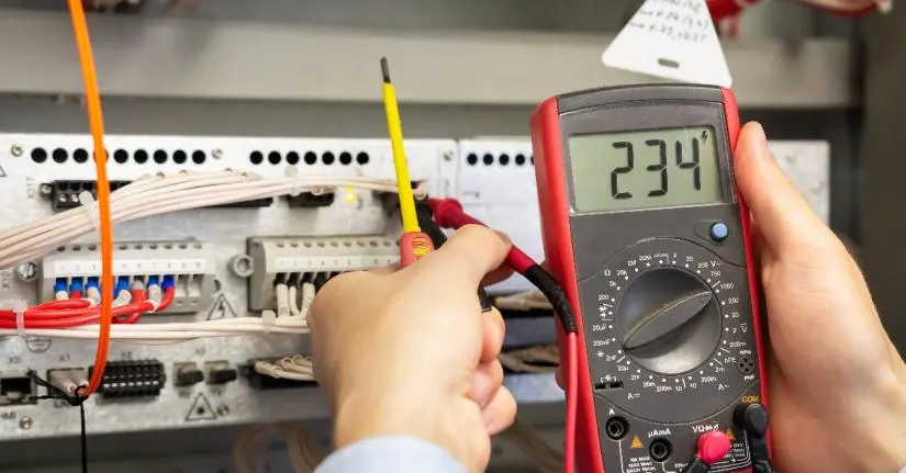 An electrician performing electrical maintenance on a panel of wires by using testing the wires with a multimeter.