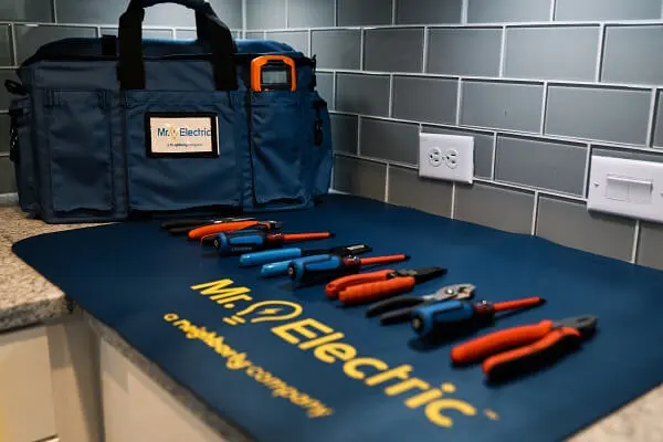  A blue Mr. Electric mat with tools on it next to a duffel bag on a counter with an outlet above it.