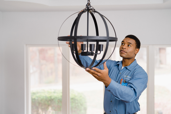 A Mr. Electric electrician installs a black lighting fixture.