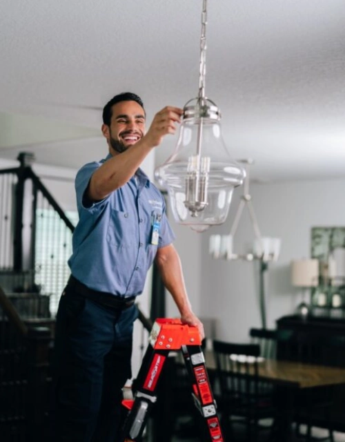 Smiling Mr. Electric technician hanging a light fixture.