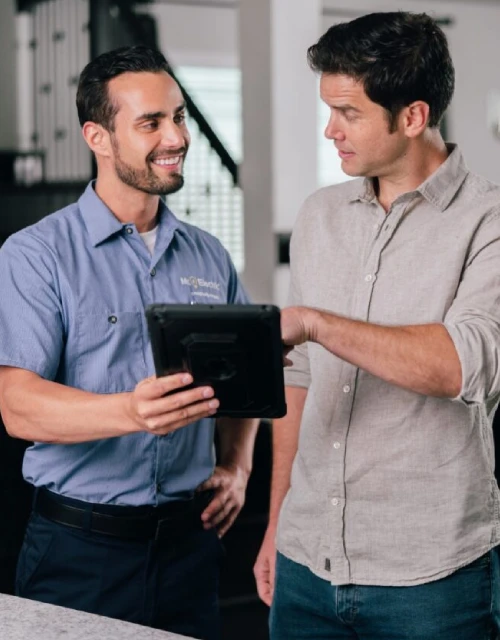 Smiling male Mr. Electric associate holding tablet device beside male customer in tan shirt.