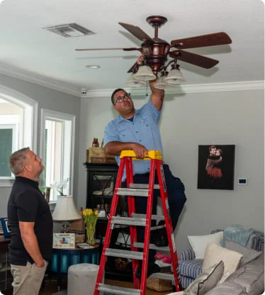 Electrician standing on ladder, working on ceiling fan.