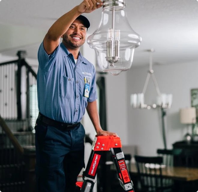 Smiling male electrician on ladder adjusting ceiling lamp inside residential home.