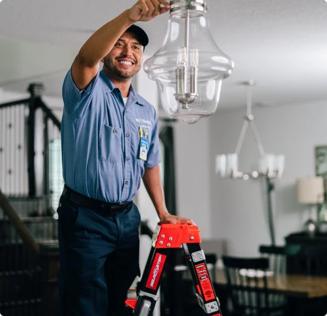 Mr. Electric electrician on a ladder adjusting ceiling lamp inside a residential home.