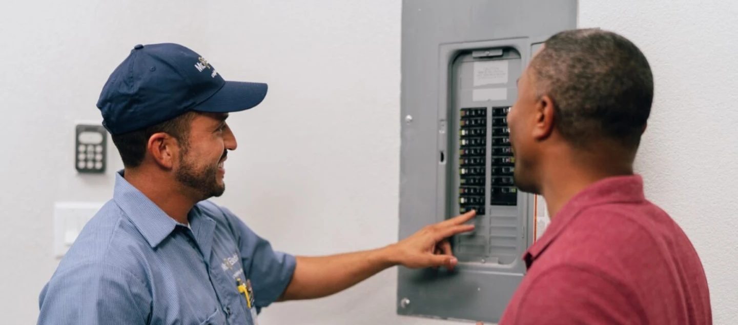 Electrician and male customer talking near circuit breaker.