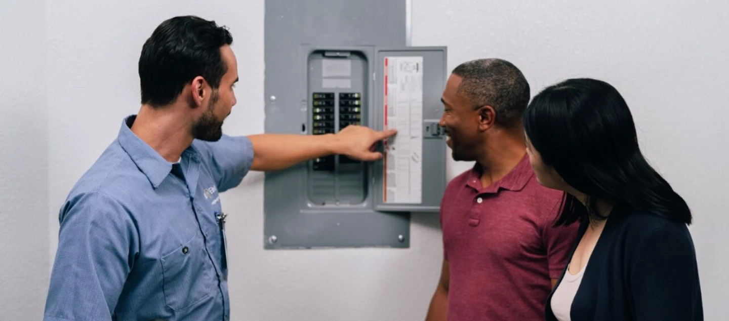 Mr. Electric electrician showing circuit breaker board to two people.
