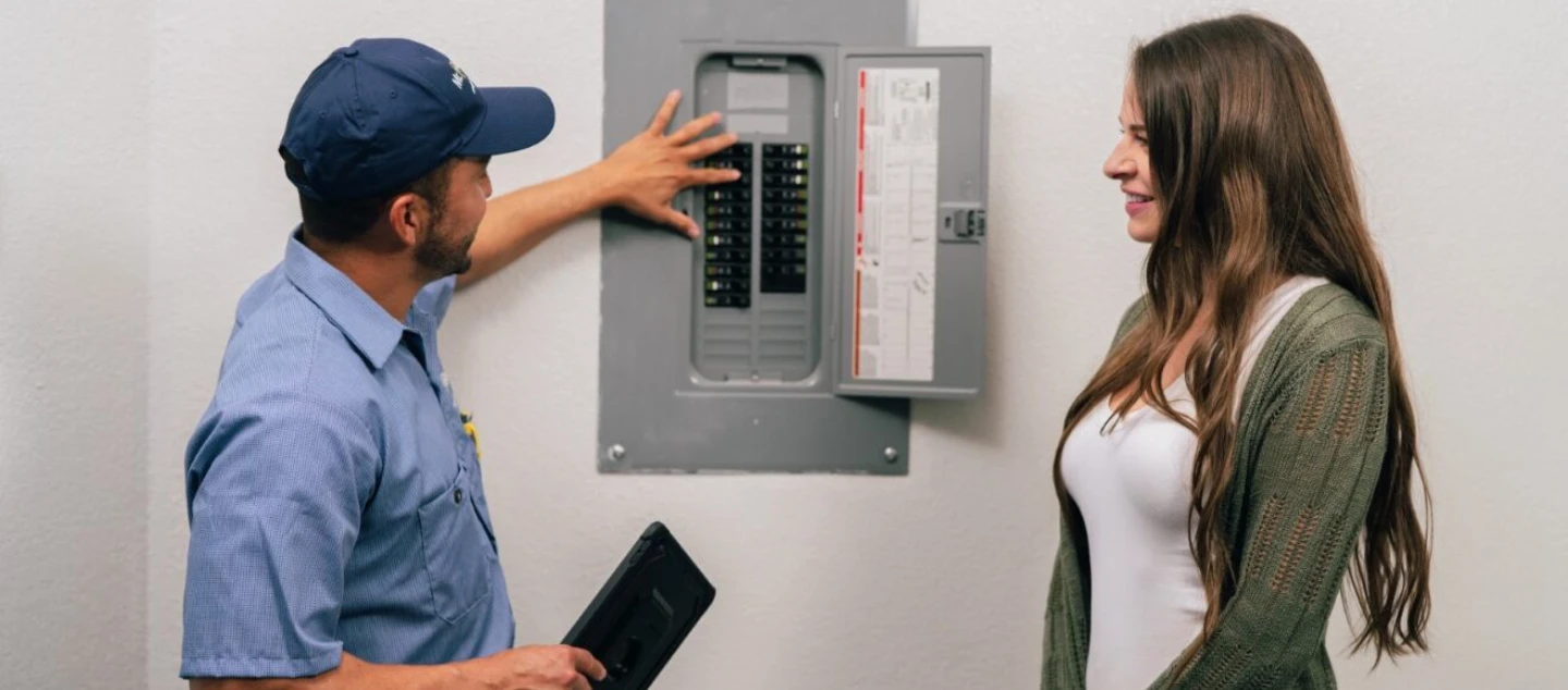Mr. Electric electrician showing circuit breaker box to female customer.