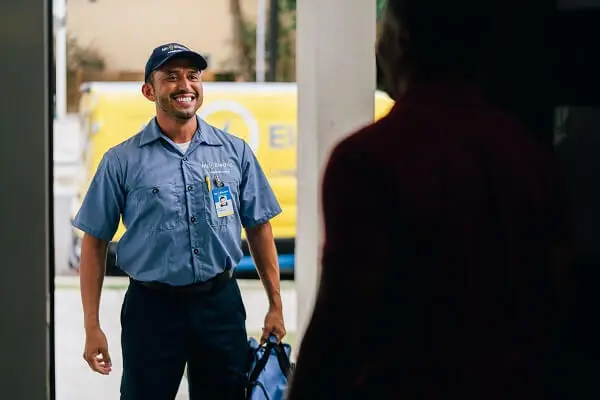 A Mr. Electric electrician in front of a door holding a bag looking at a man inside the doorway. 