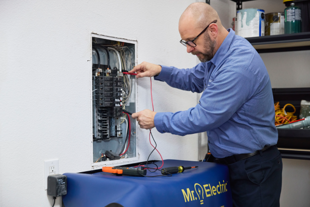 MRE Electrician working on a circuit breaker panel, using a multimeter to test electrical connections.