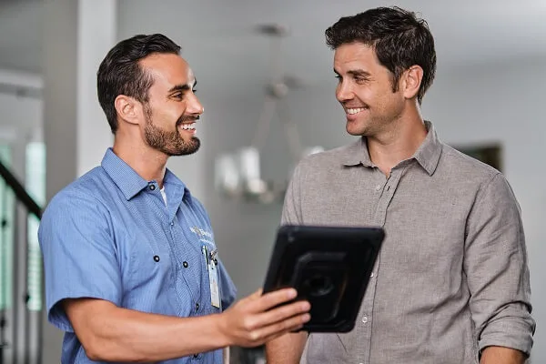 A smiling Mr. Electric electrician shows something on a tablet to a smiling man next to him.