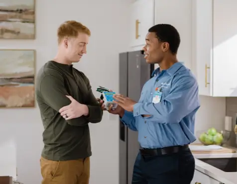 Electrician in a blue button-down shirt discussing wiring updates and code compliance, holding electrical wires while talking to a homeowner in a modern white kitchen.