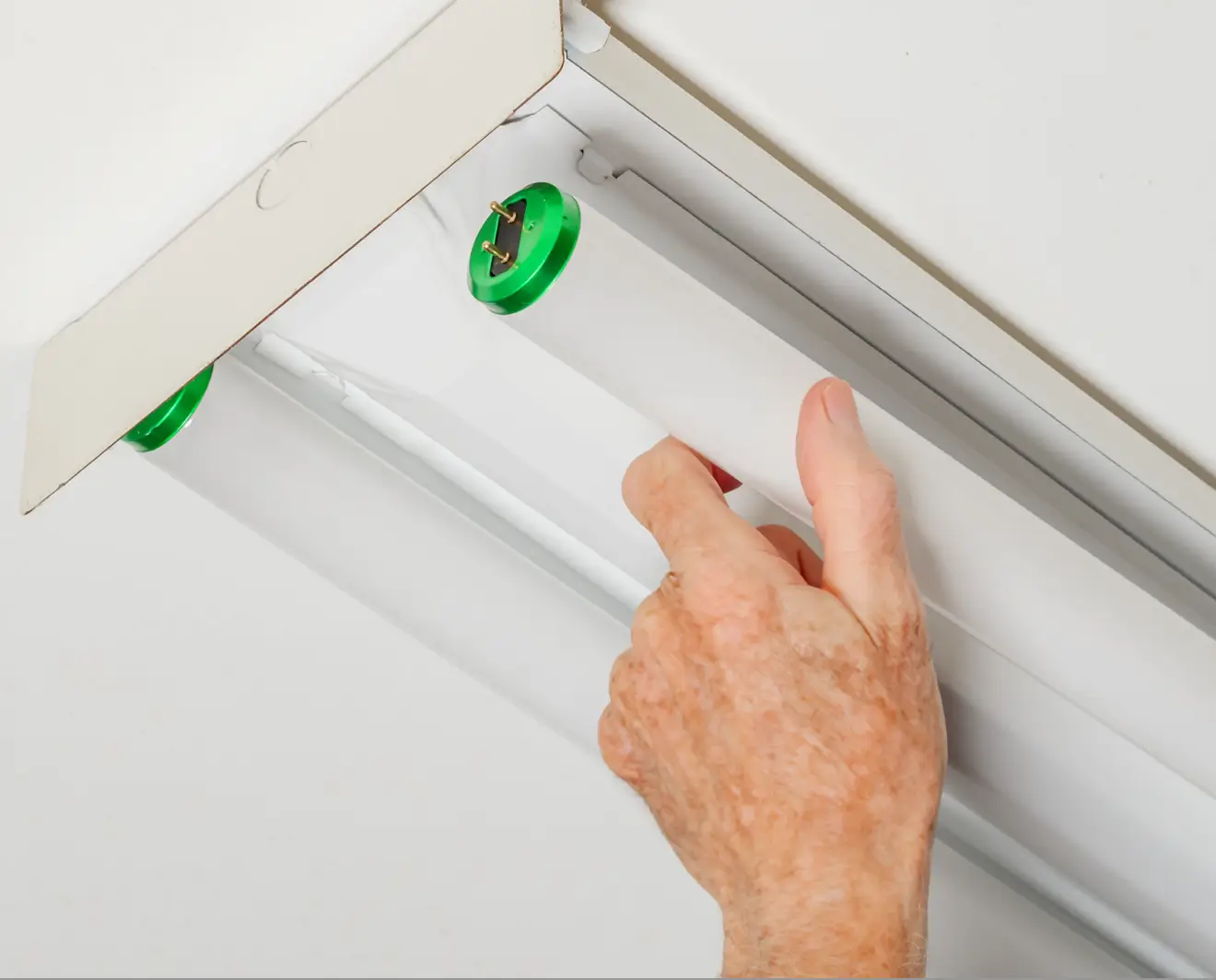 Close-up view of a hand installing or removing a fluorescent light tube with green end caps into a ceiling fixture, focusing on electrical maintenance process.