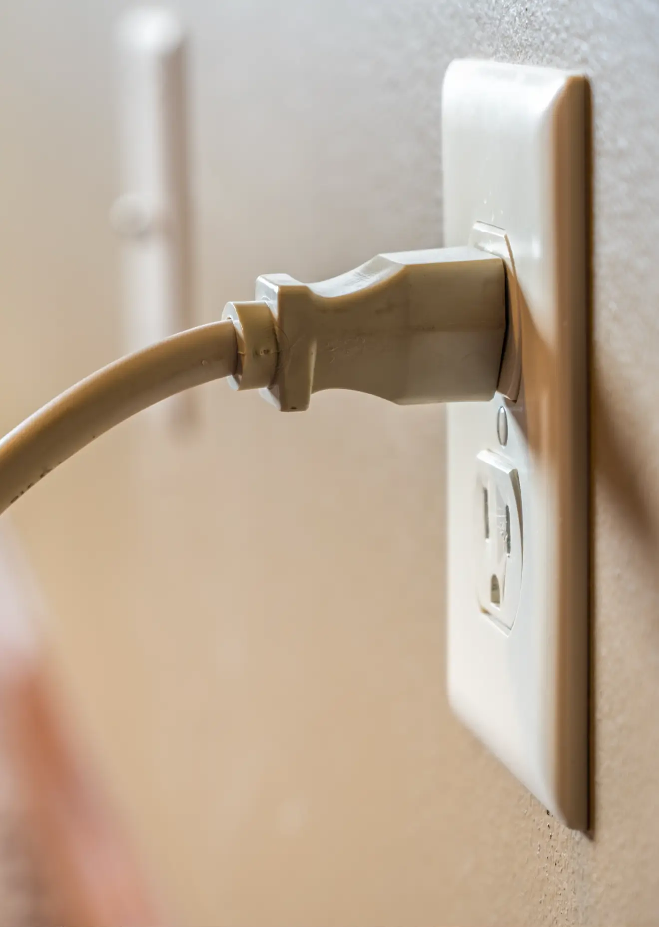 Close-up of a thick white power cord securely plugged into a standard wall electrical outlet in a home environment.
