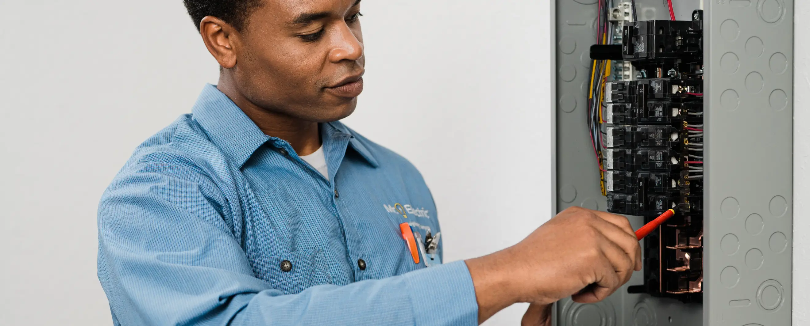 Service professional in a blue shirt adjusting wiring inside a residential electrical breaker panel, focusing intently on the components.