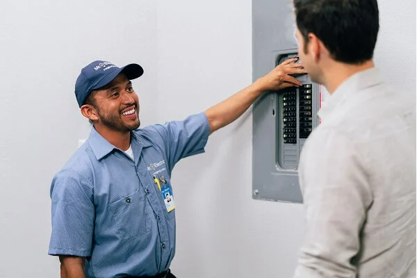 A smiling Mr. Electric service professional points at an open electrical panel while talking to a man.