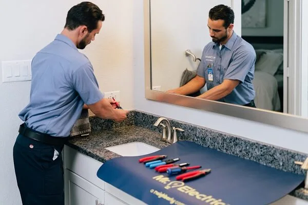 A Mr. Electric service professional at a bathroom vanity working on an outlet.