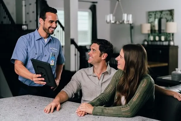 A smiling Mr. Electric electrician shows a tablet to a seated couple at a counter next to him.