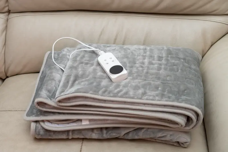 A folded electric blanket with the remote control sitting on top.