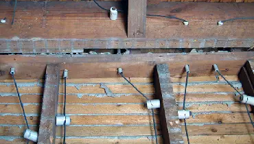 white ceramic knobs attached to joists and white ceramic tubes through joists, with wires running through knobs and tubes