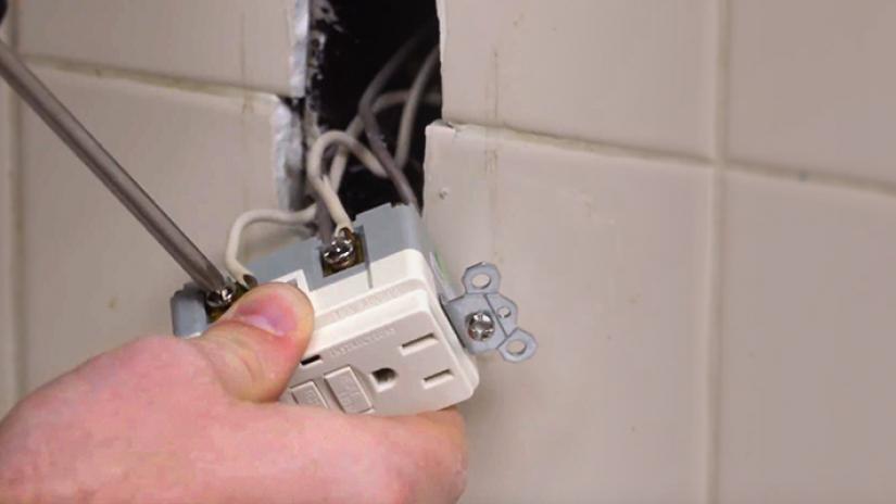 Person attaching wires to a GFCI outlet on a white tiled wall