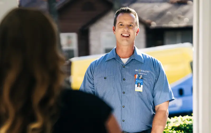 A Mr. Electric service professional approaching the front door of a house greeting the homeowner.