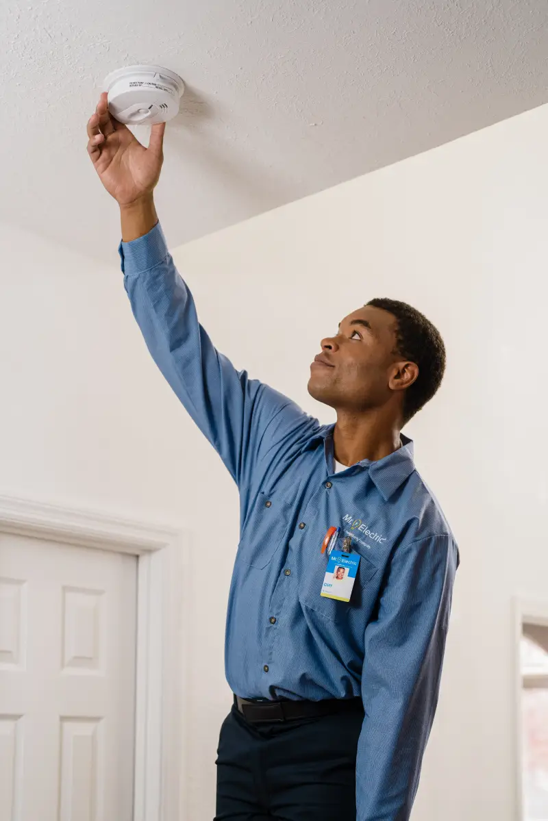 A Mr. Electric service professional inspecting a smoke detector.