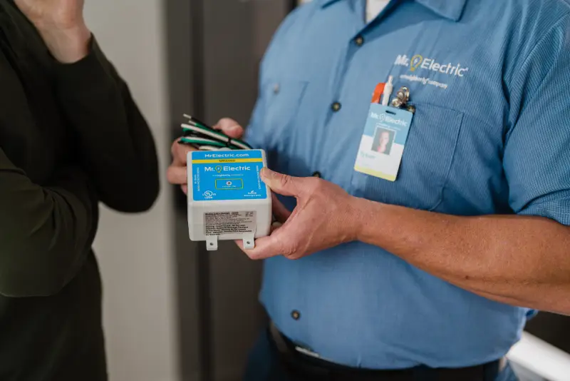 A Mr. Electric service professional holding a surge protection device.