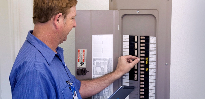 A technician in a blue shirt flipping a switch on a breaker box.