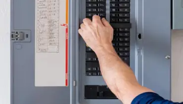 Person resetting a circuit breaker on residential electrical panel.