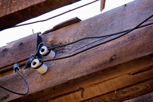 Close-up of a knob and tube wiring setup, with ceramic knobs and insulated, exposed wires running along a joist