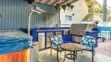 Panorama high angle view of a stylish outdoor kitchen on a brick patio with a built in gas BBQ and dining table with hanging chandelier.