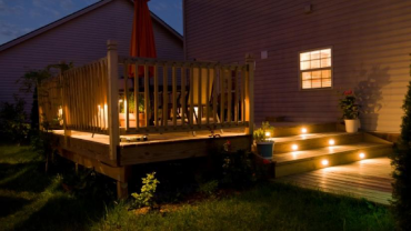 Beautiful wooden deck and patio lit up at night.